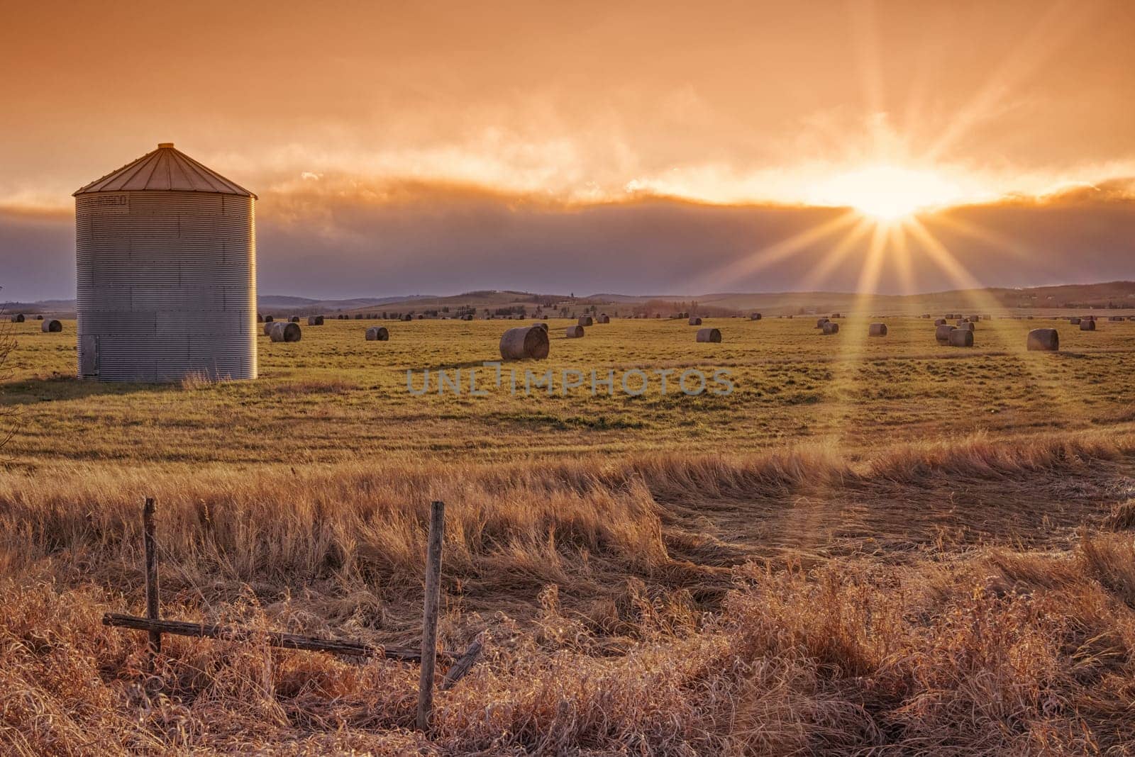Landscape of the setting sun on the prairie with a grain elevator and sunburst.