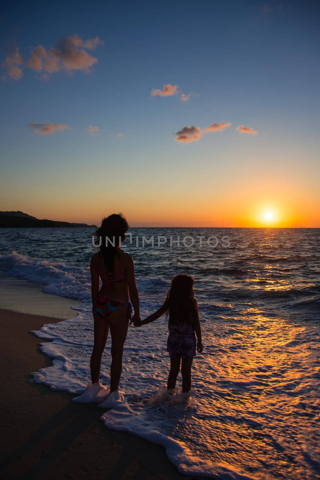 mother and daughter watching the sunset standing on the beach