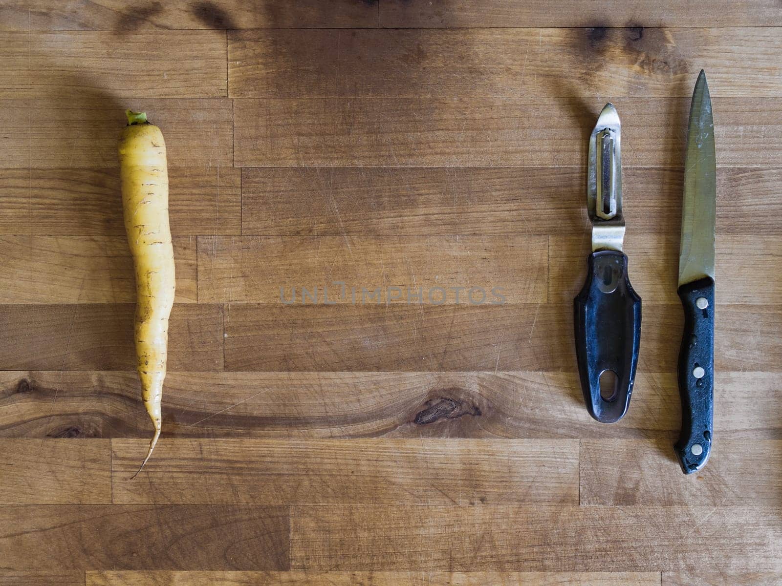 Yellow carrot, knife and peeler on a wooden board, meal preparation scene, cooking background