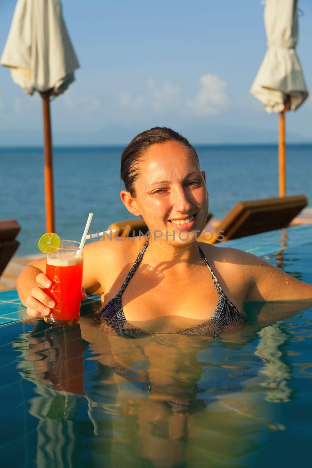 Young woman drinking Mai Thai Cocktail at the pool in a family hotel in Ko Samui, Thailand