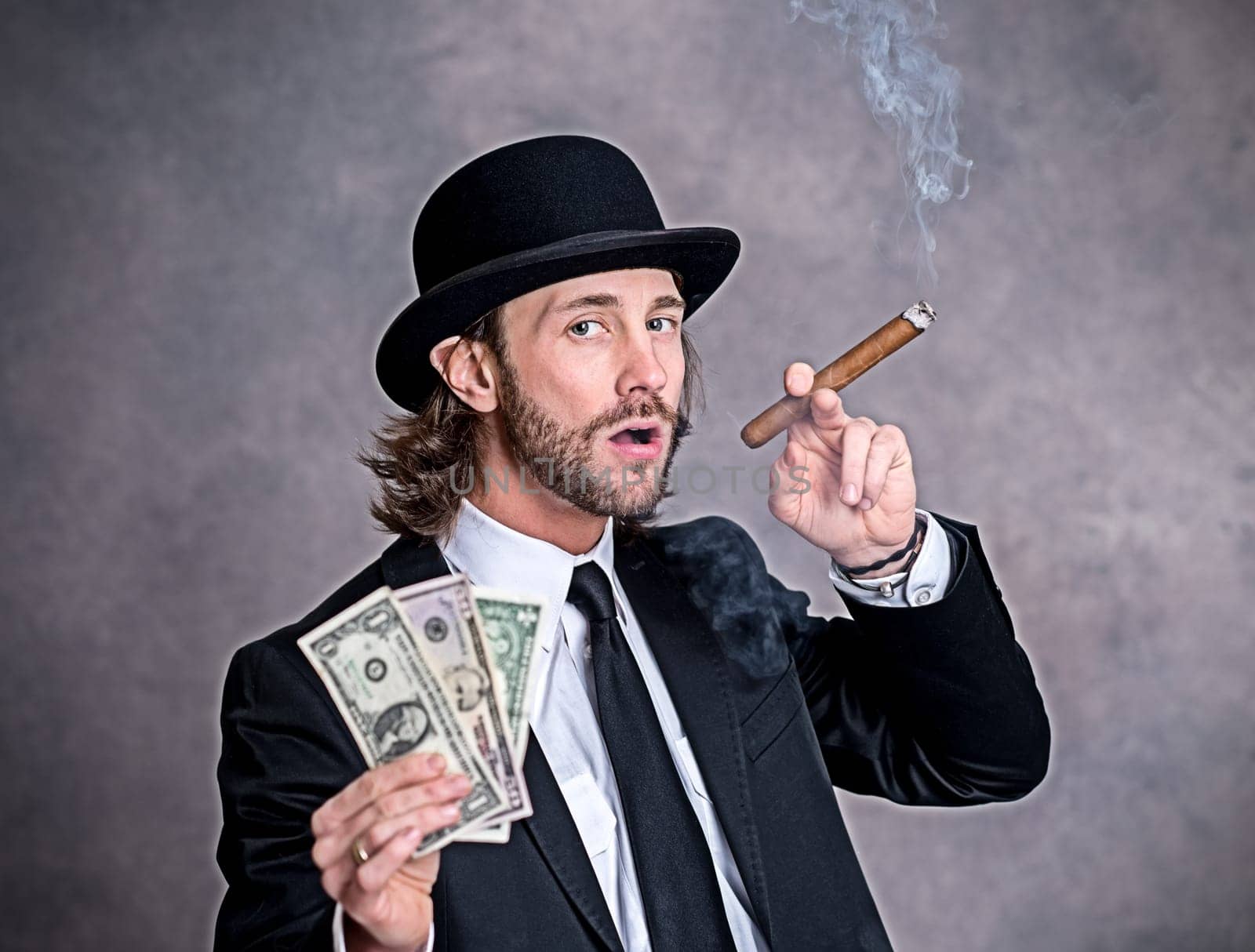 young businessman with bowler hat in black suit showing money and smoking big cigar