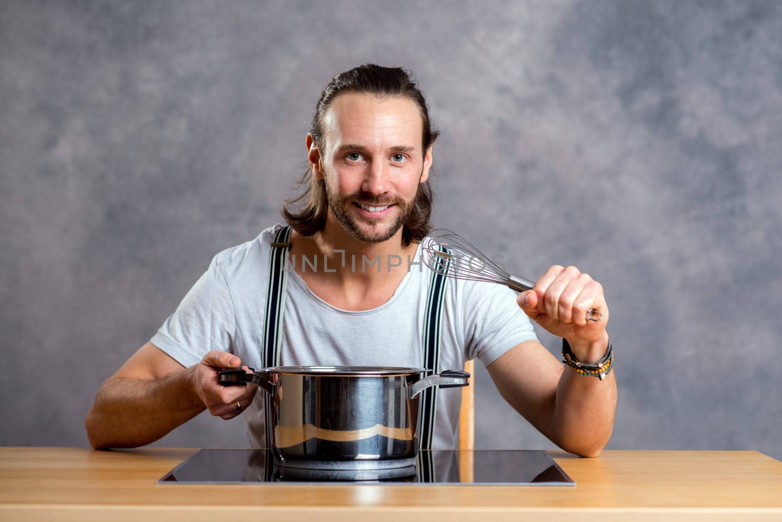 young bearded man with cooking pot in front of gray background