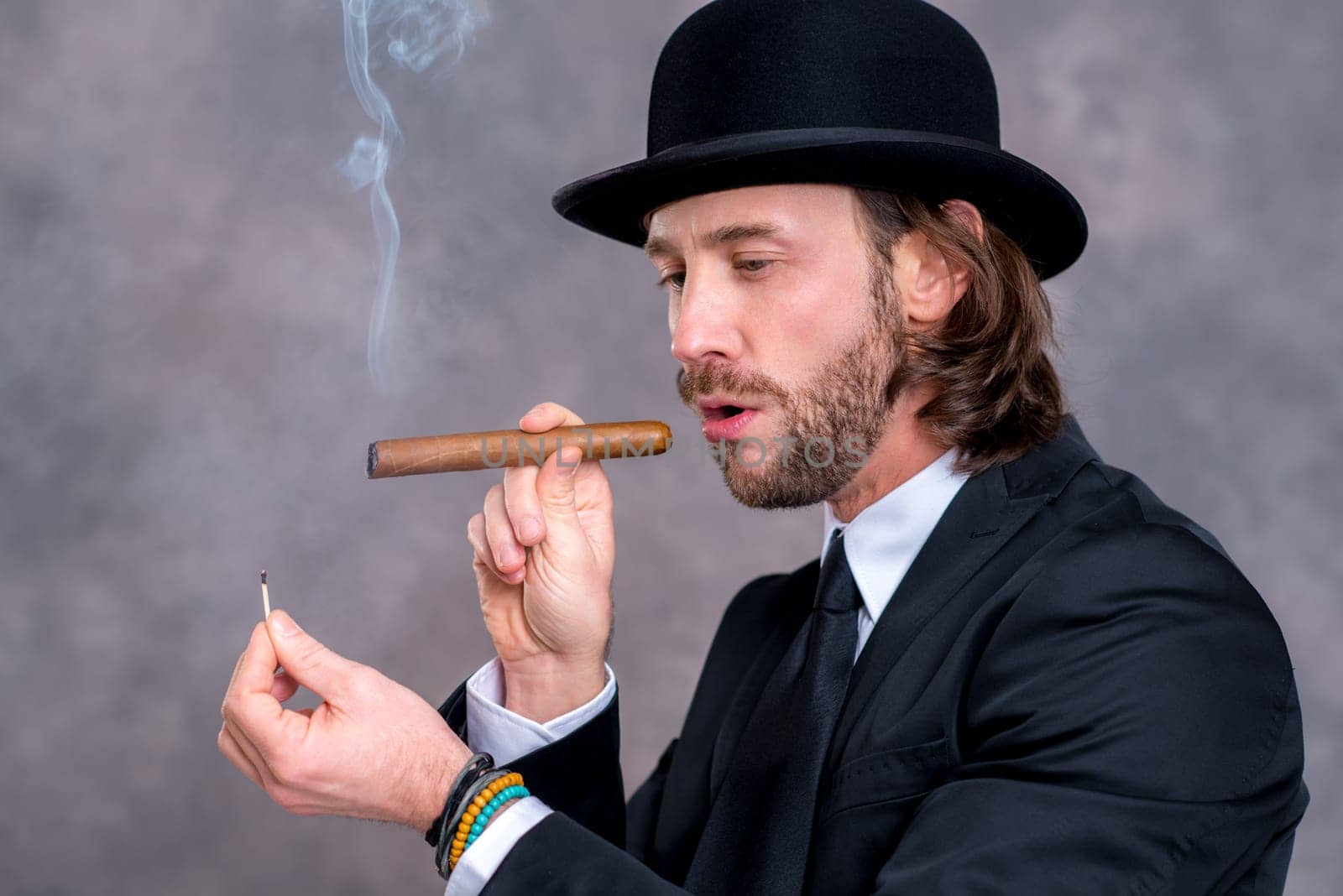young businessman with bowler hat in black suit smoking big cigar