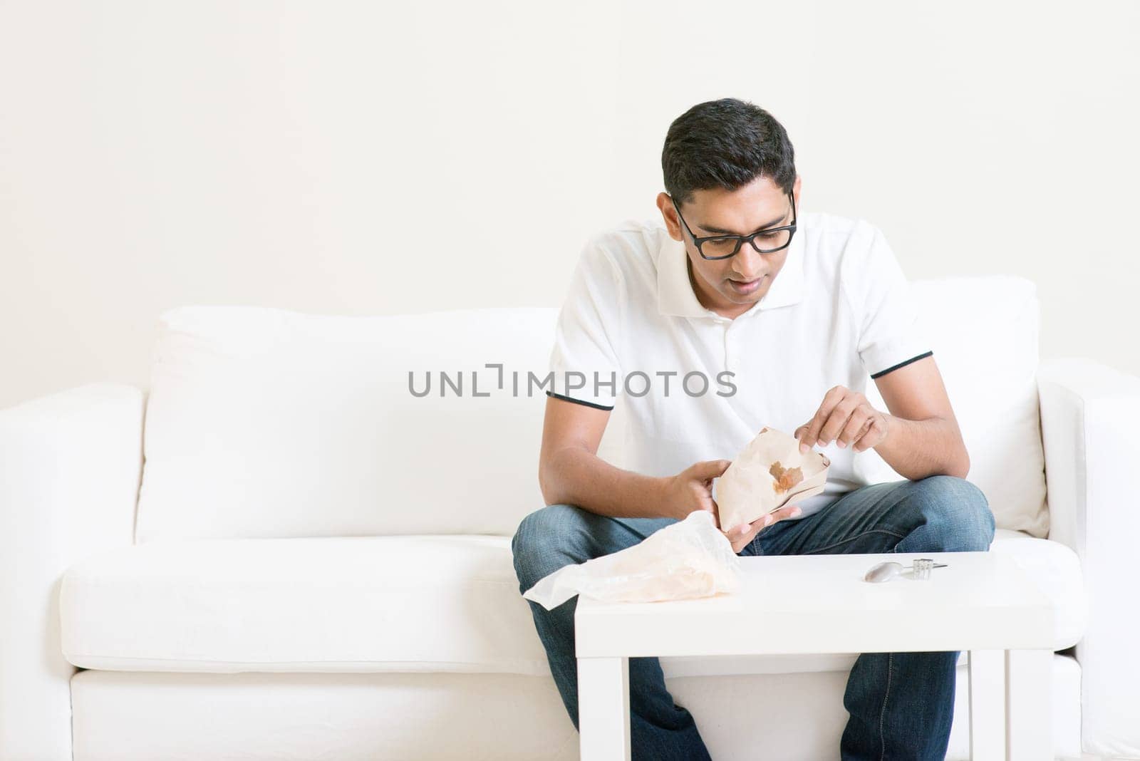 Lonely young single Asian Indian man eating food alone at home, copy space at side. Having nasi lemak as lunch.