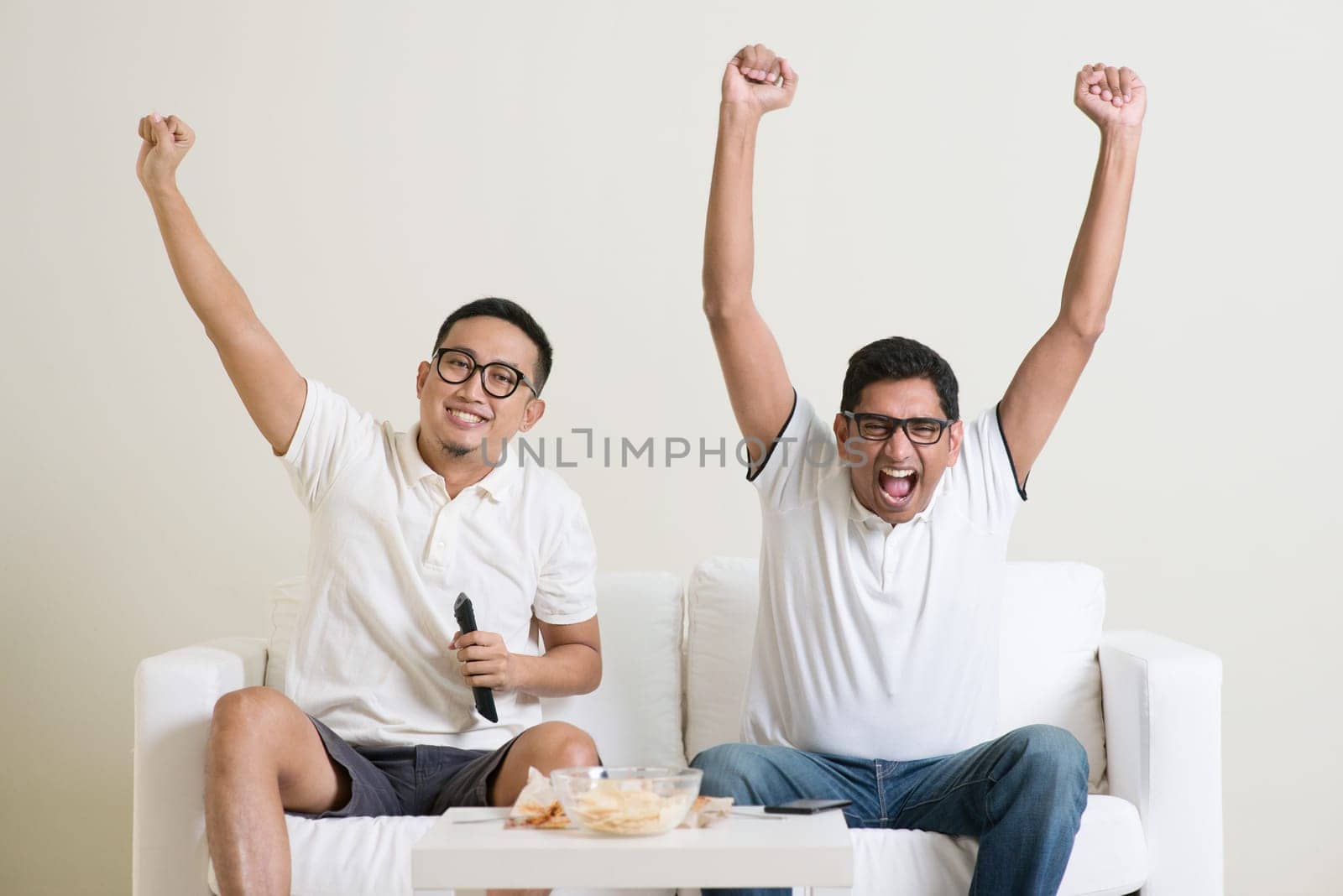 Cheerful group of friends watching football game on tv at home.