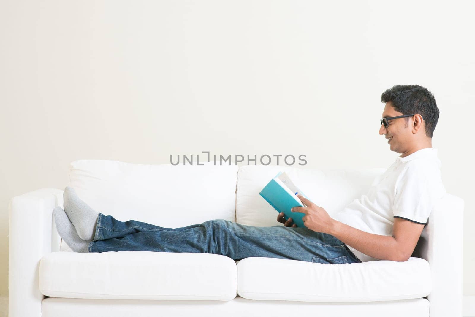 Young single Indian guy reading book and rest at home. Asian man relaxed on sofa indoor. Handsome male model.