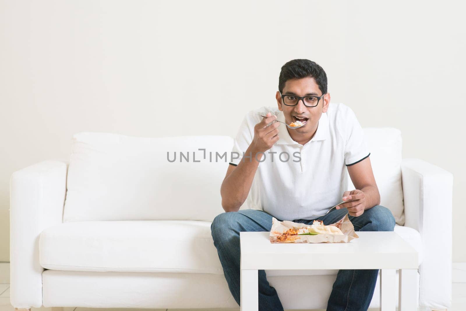 Lonely young single Indian man eating food alone, copy space at side. Having nasi lemak as lunch. Lifestyle of Asian guy at home.