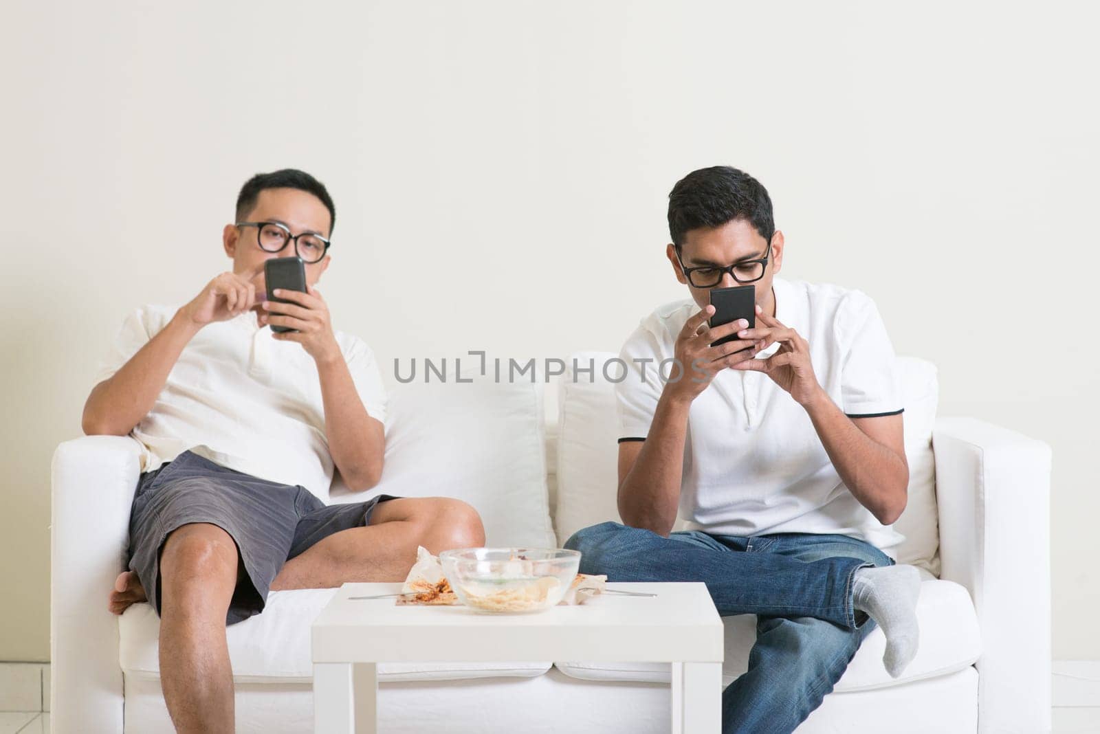 Friends sitting on sofa and playing on their phones at home.