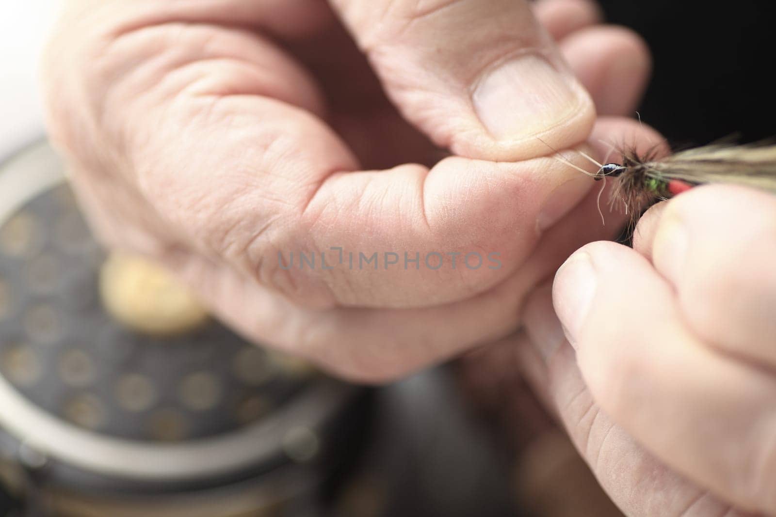 Closeup view of a man holding an imitation insect artificial fly, fishing reel in background