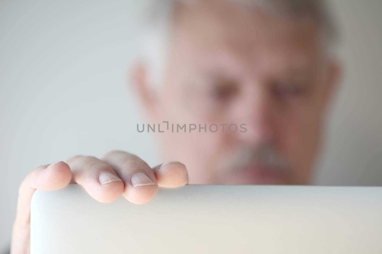 Older man has hand on his laptop, face defocused