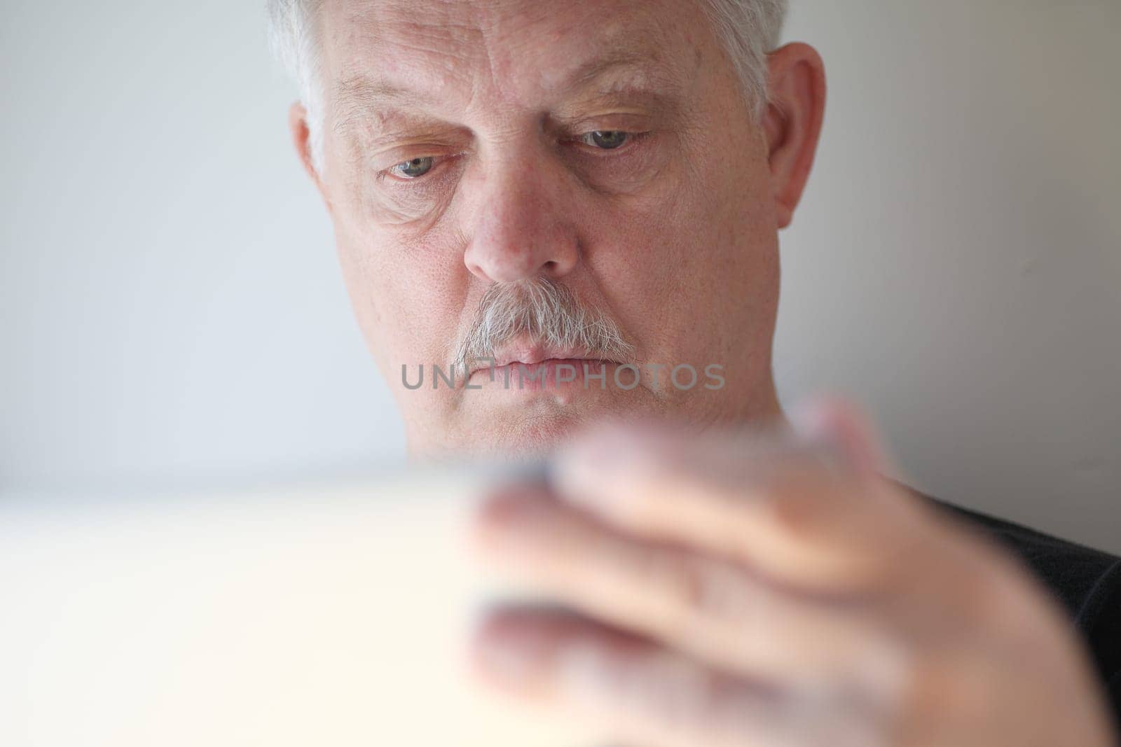 A senior man with a hand on his laptop cover checks his screen.