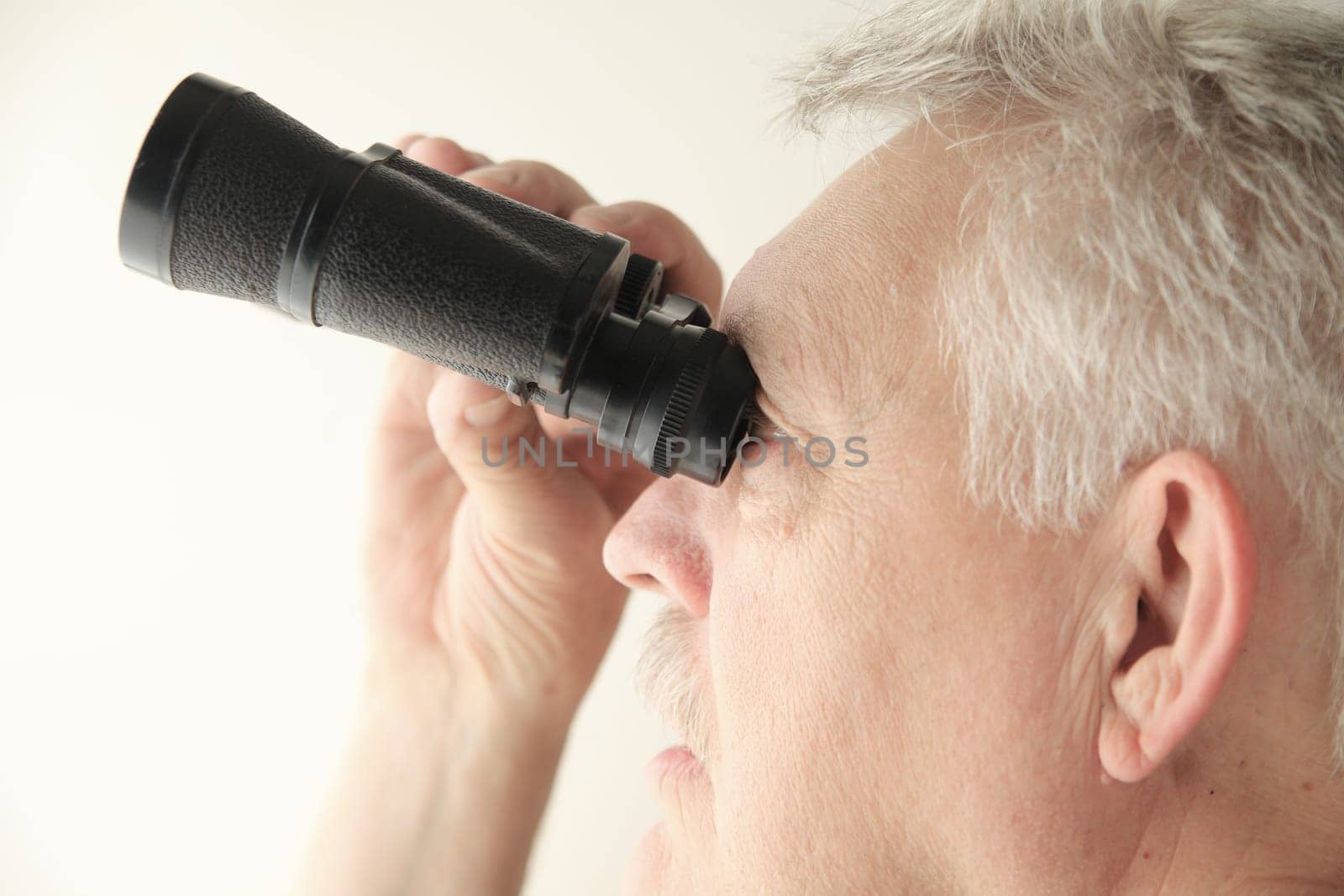 Senior man looking upward with an old pair of binoculars, copy space included.