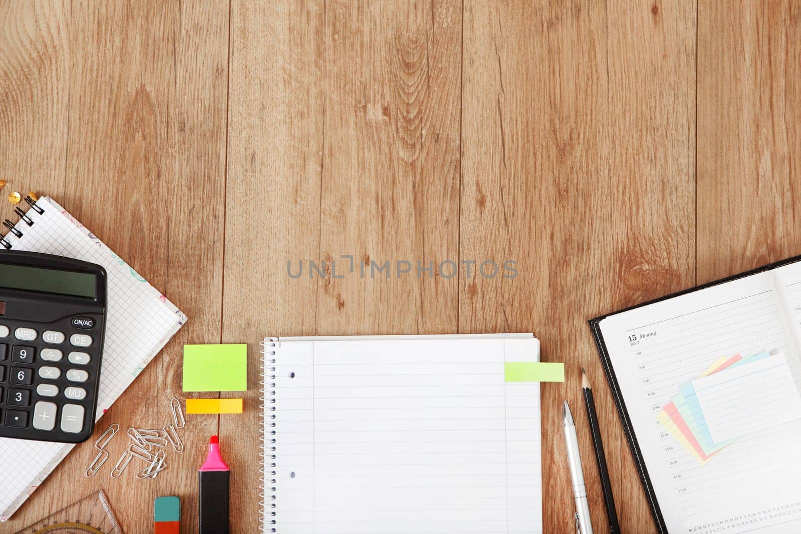 a calendar and a notepad lie on a desk with pens and calculator