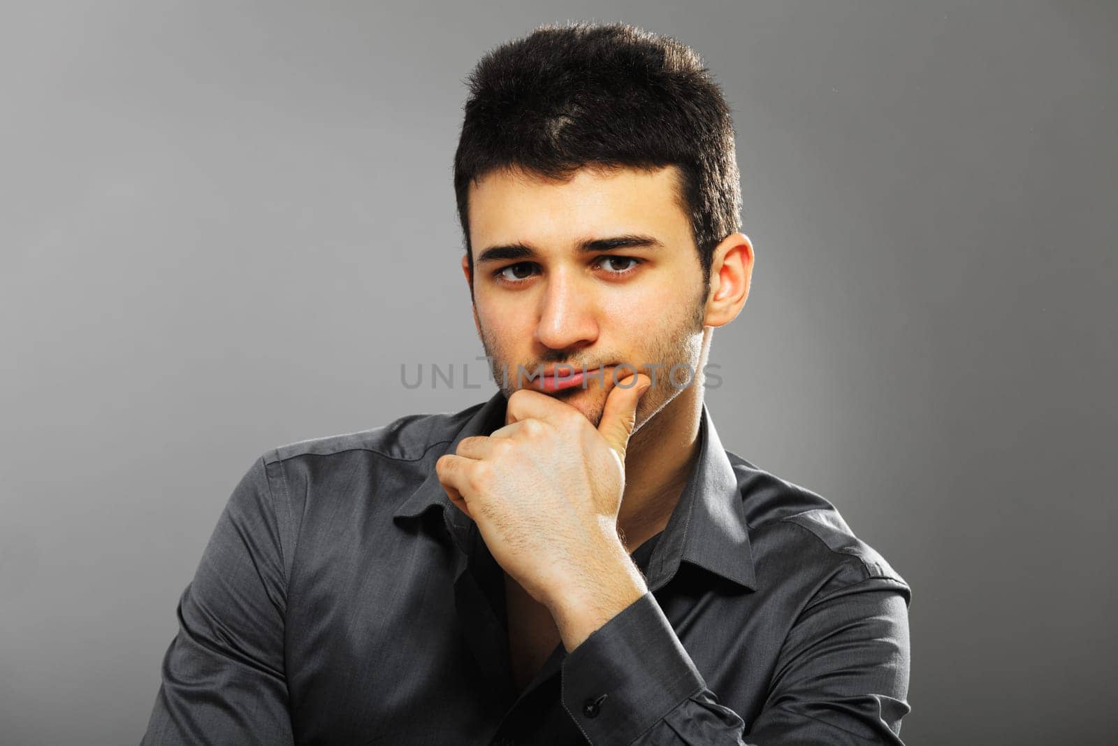 Young businessman portrait isolated on gray background. Hand on chin