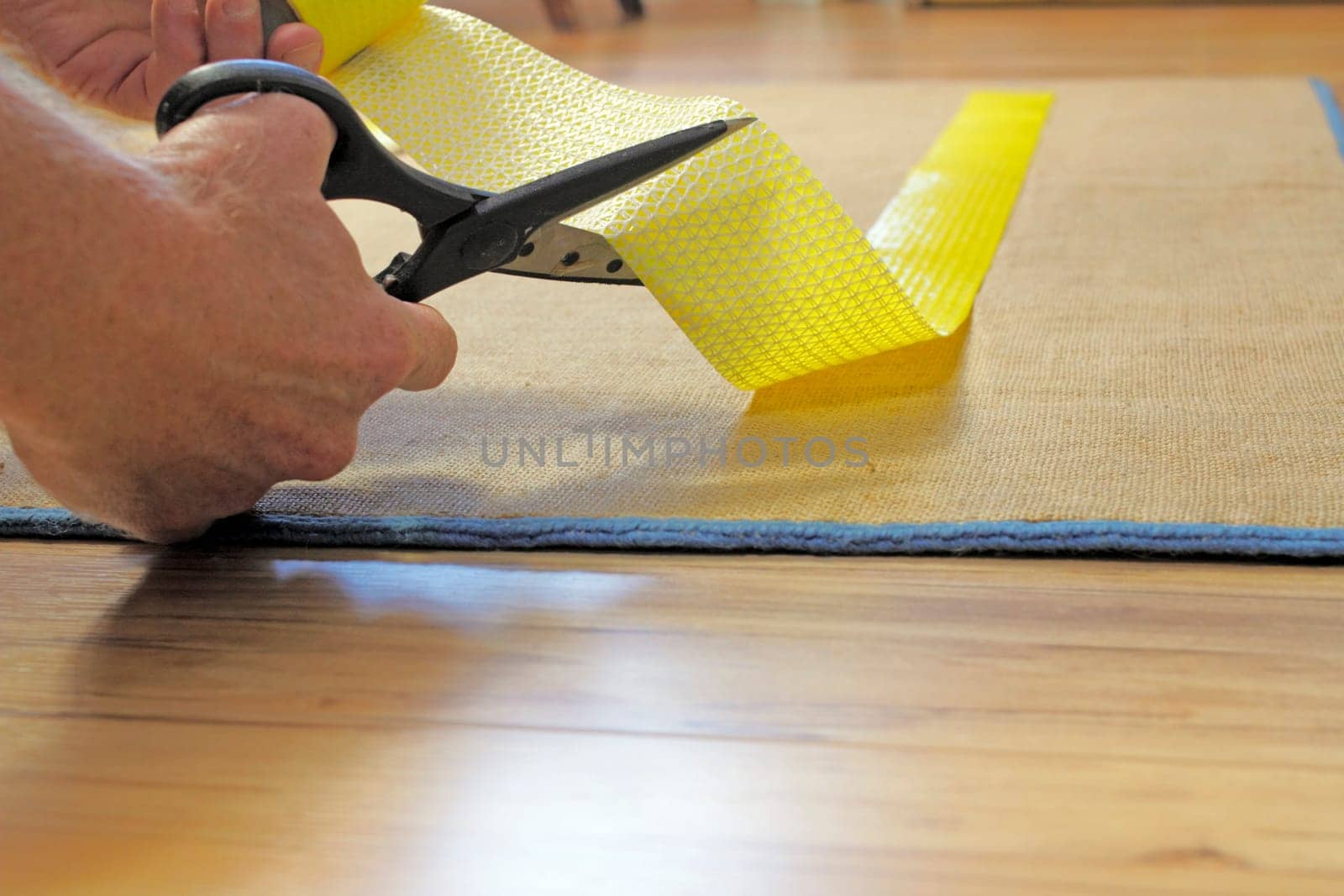 Male caucasian hands with black handle stainless steel scissors cutting to size a strip of yellow anti-slip rug grip tape. Cutting and placing anti-skid carpet tape.