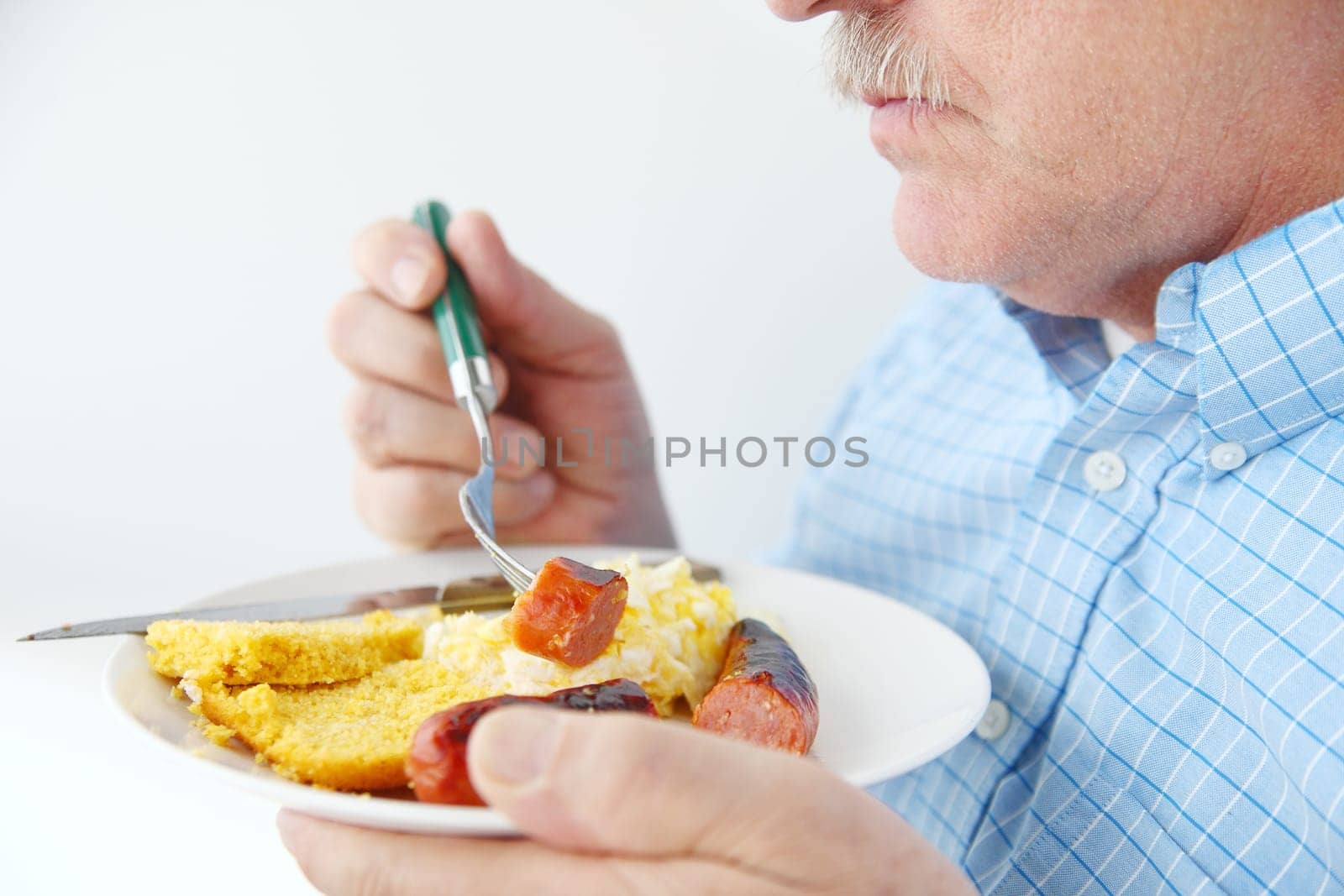 A man eating sausage, scrambled eggs and cornbread for breakfast