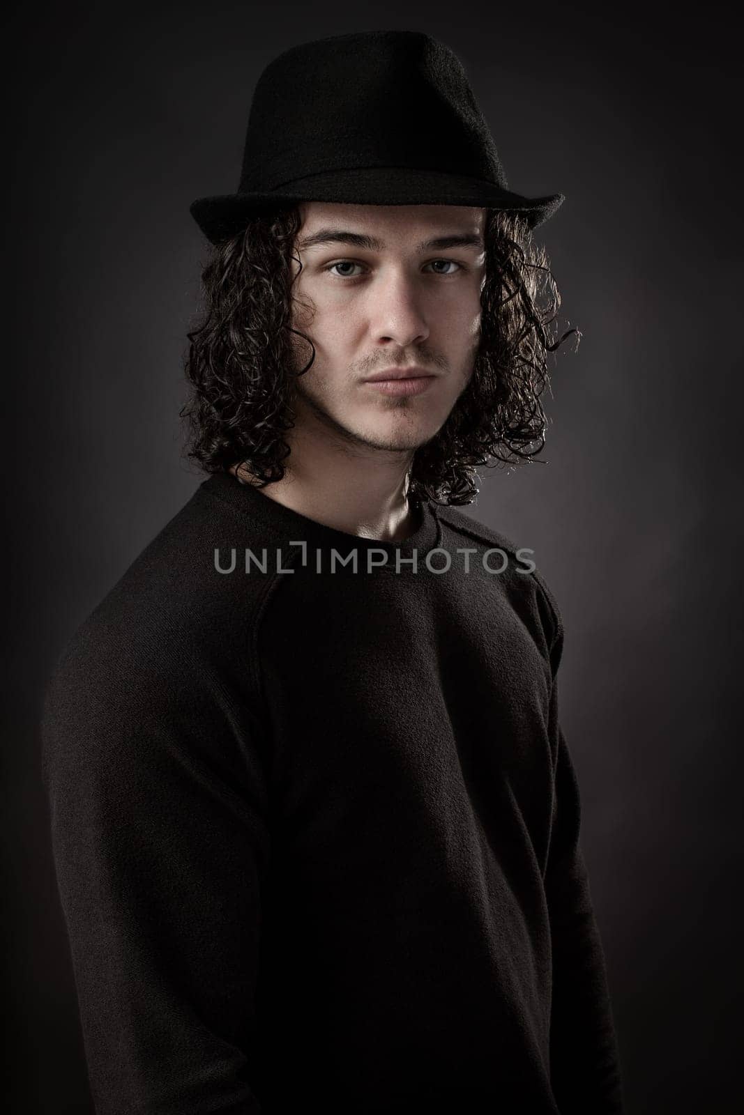 Portrait of young man dressed in black with long hair and hat