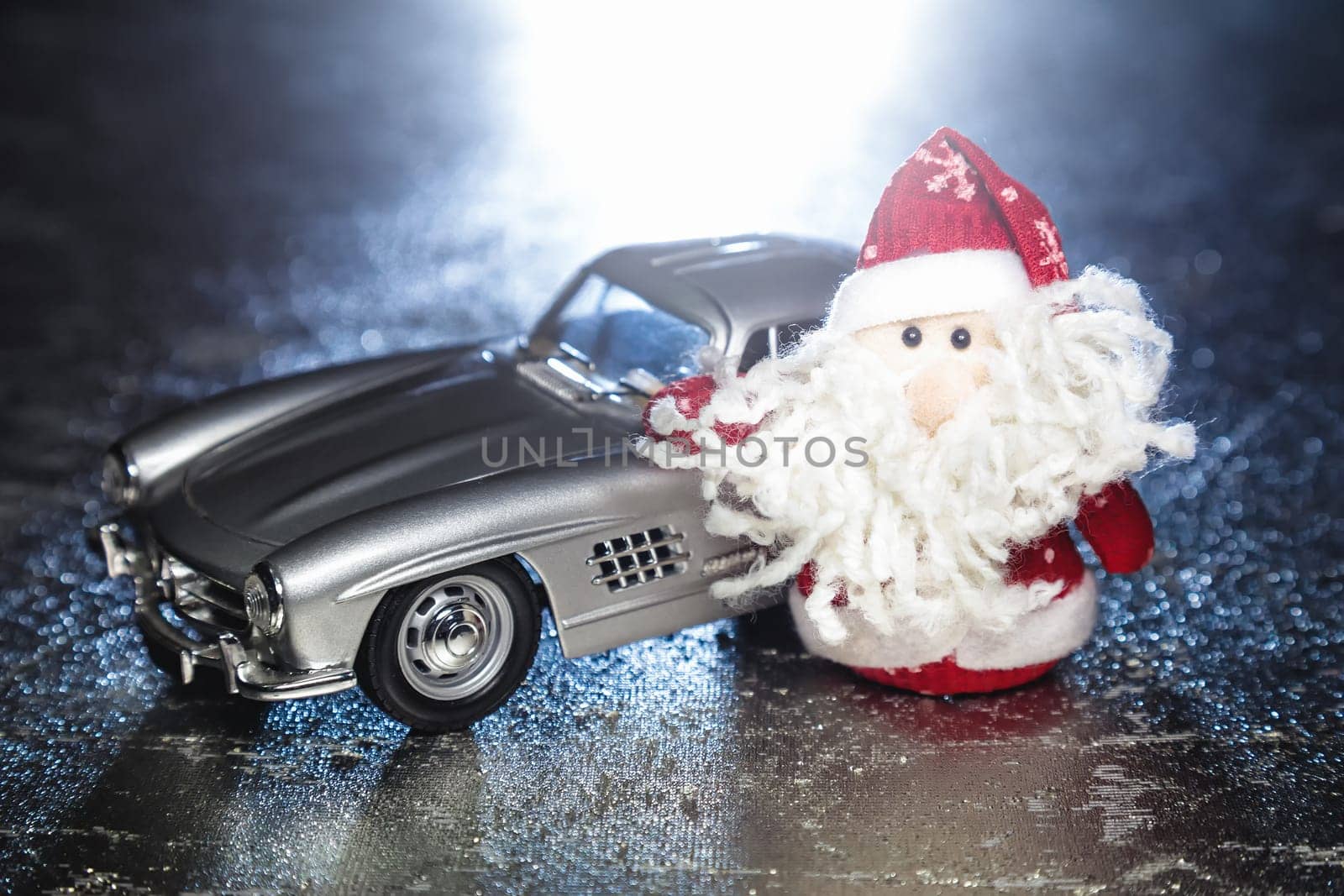 Santa Claus or Father Frost with old vintage automobile on on silver or metal grunge surface with backlight from behind. Main focus of image on Santa Claus and selective on turned left toy retro car