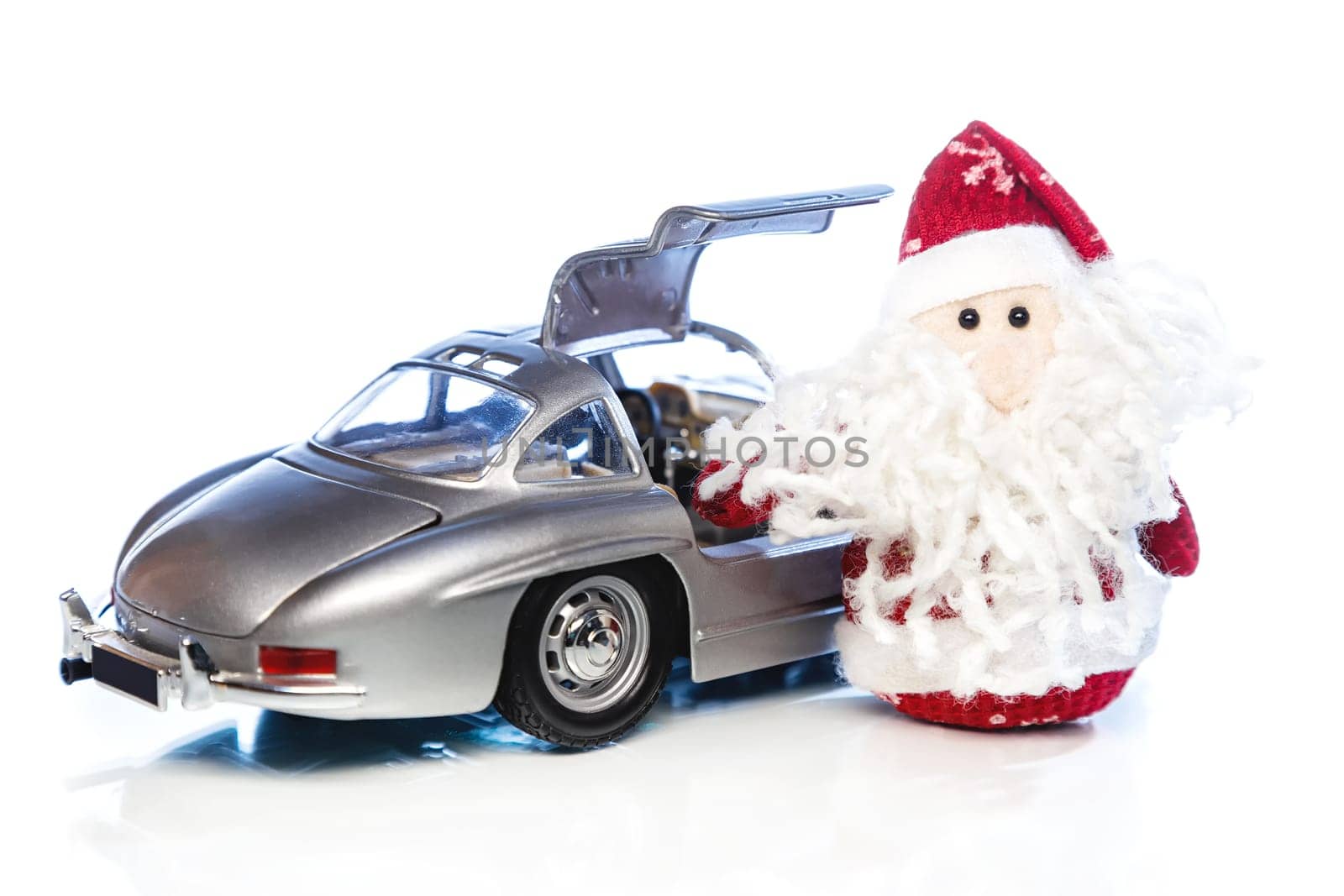 Santa Claus or Father Frost with old vintage automobile on white background with reflection. Main focus of image on Santa Claus and selective on turned the back side and opened right door toy retro car