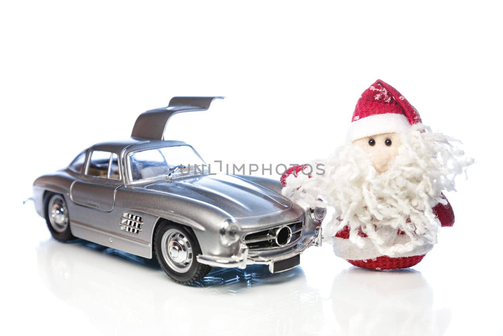 Santa Claus or Father Frost with old vintage automobile on white background with reflection. Main focus of image on Santa Claus and selective on turned right and opened door toy retro car
