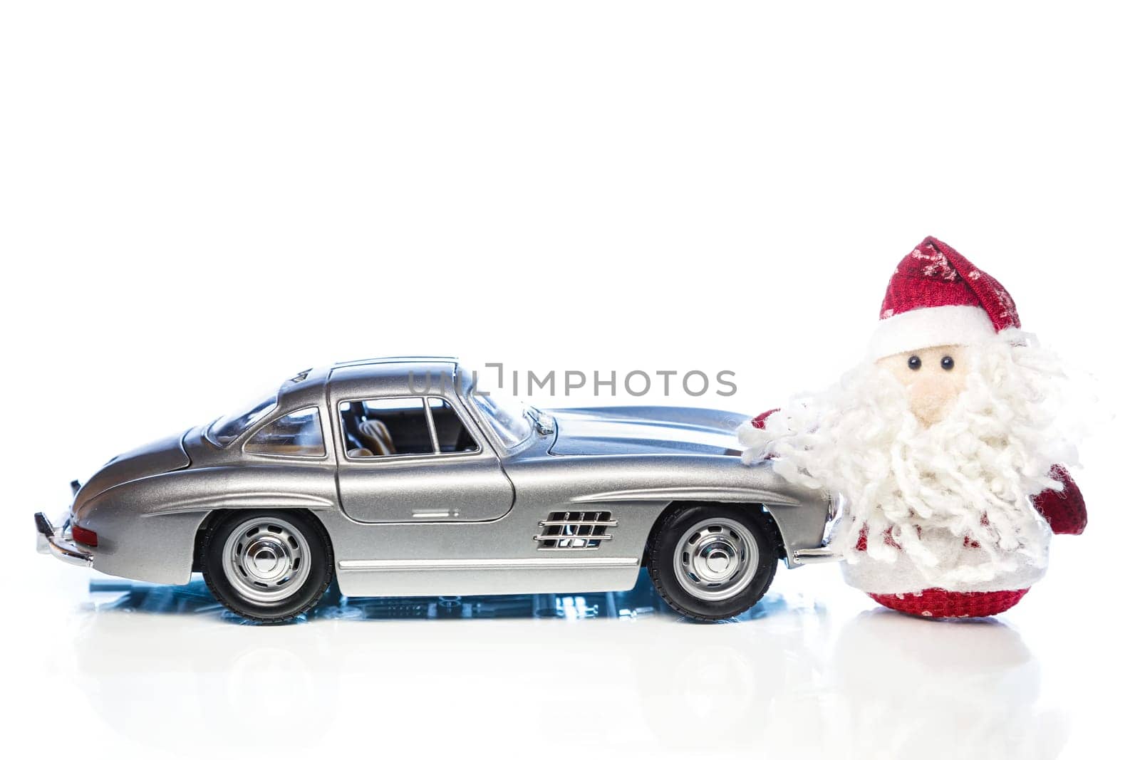 Santa Claus or Father Frost with old vintage automobile on white background with reflection. Main focus of image on Santa Claus and selective on the side turned toy retro car