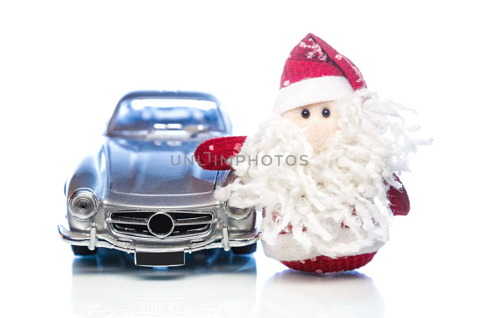 Santa Claus or Father Frost with old vintage automobile on white background with reflection. Main focus of image on Santa Claus and selective on face standing toy retro car