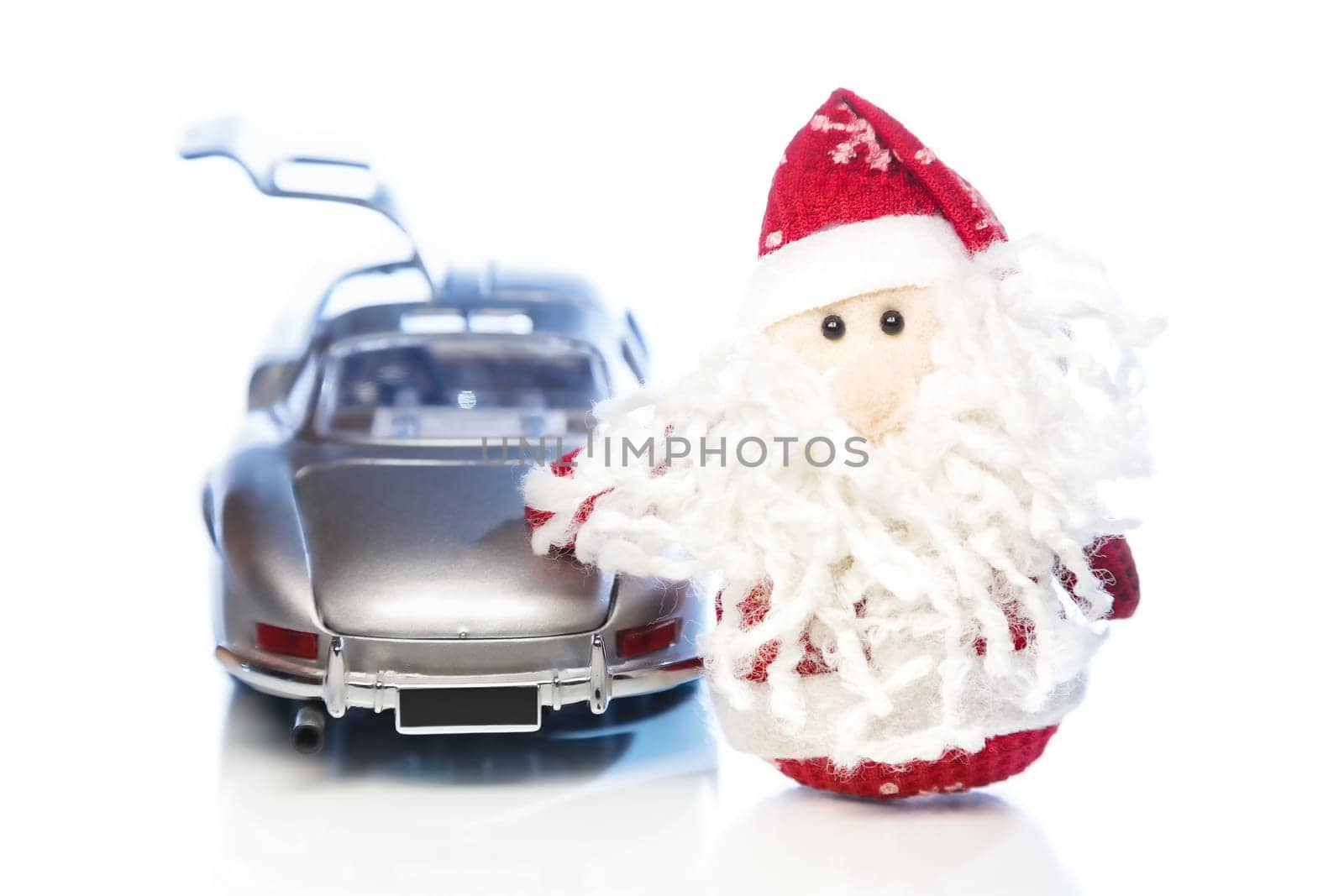 Santa Claus or Father Frost with old vintage automobile on white background with reflection. Main focus of image on Santa Claus and selective on turned the back side and opened left door toy retro car