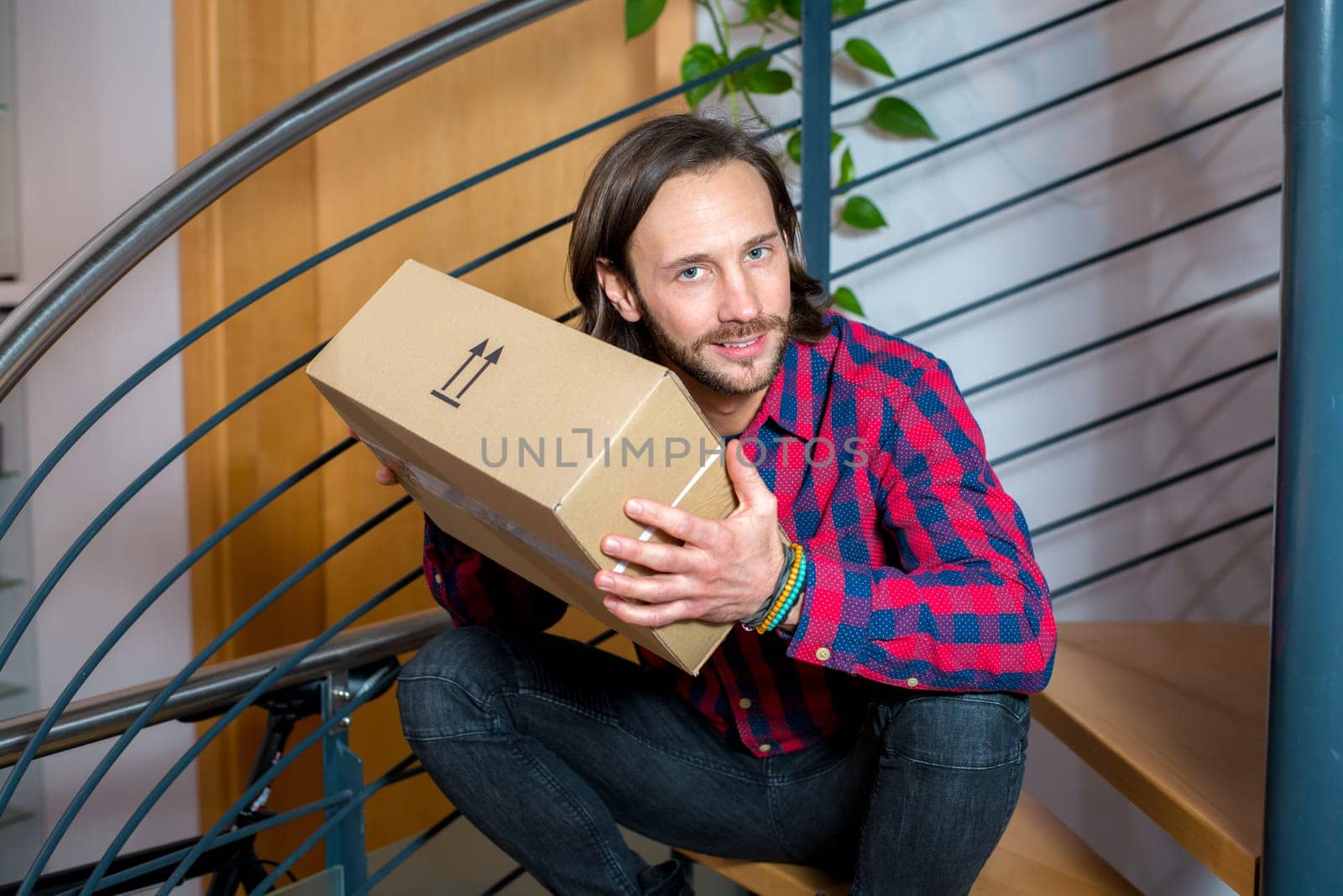 young man sitting in corridor and opening a package