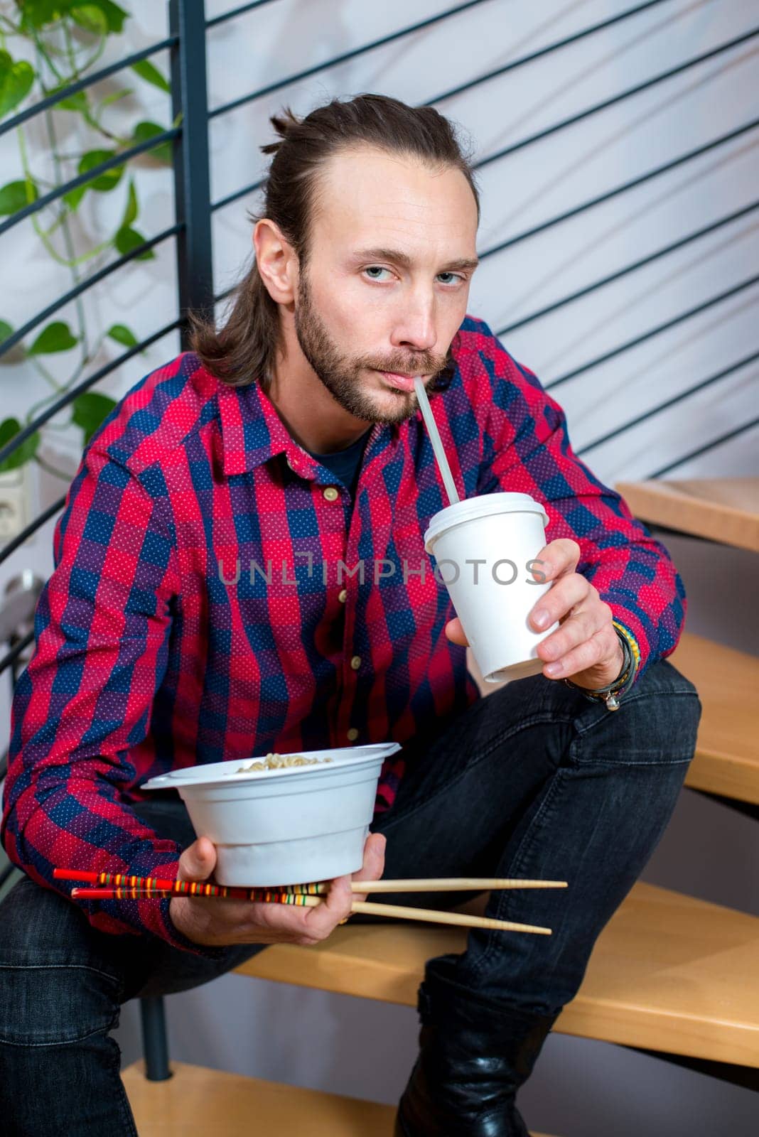 young man in checkered shirt sitting on stairs and eating asian food