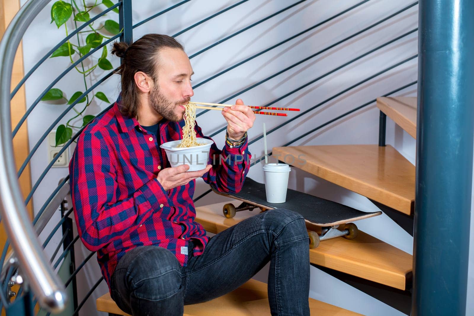 young man in checkered shirt sitting on stairs and eating asian food