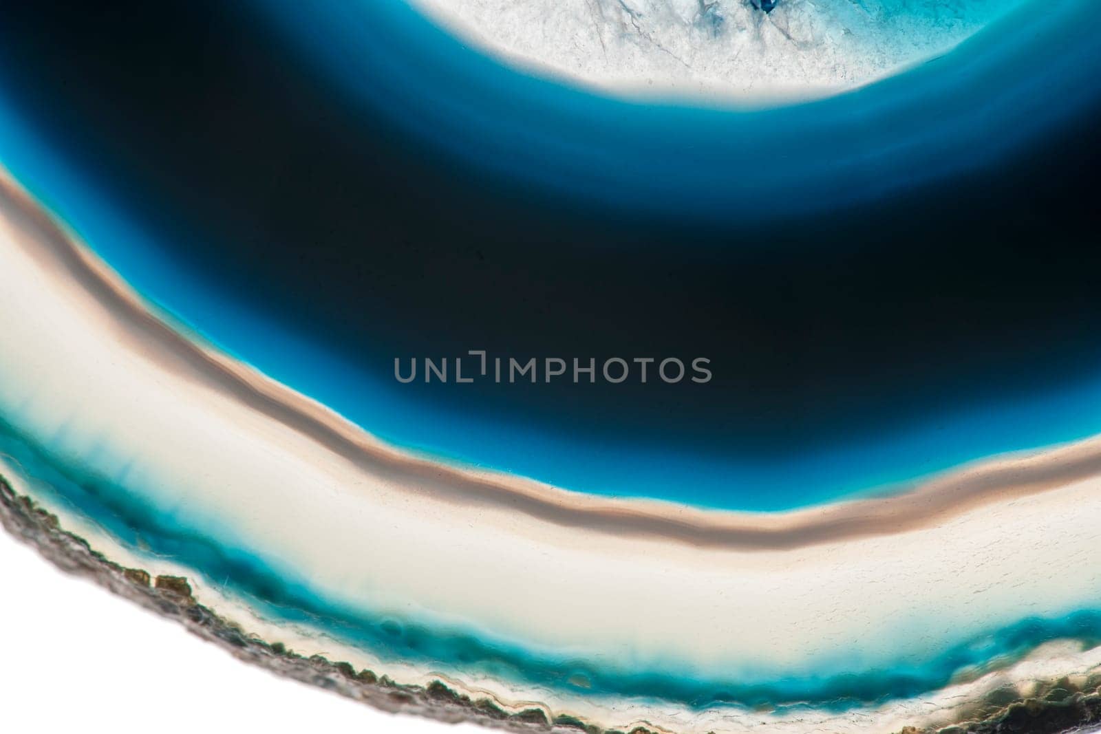 Close-up of a part of a flat,polished and transparent disc of an agate with round structures similar to the annual rings of a tree in blue and green with crusty edge insulated on white