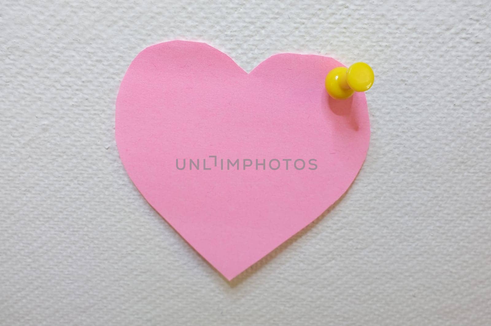 Note paper in heart shape with yellow pin posted on white cork board background