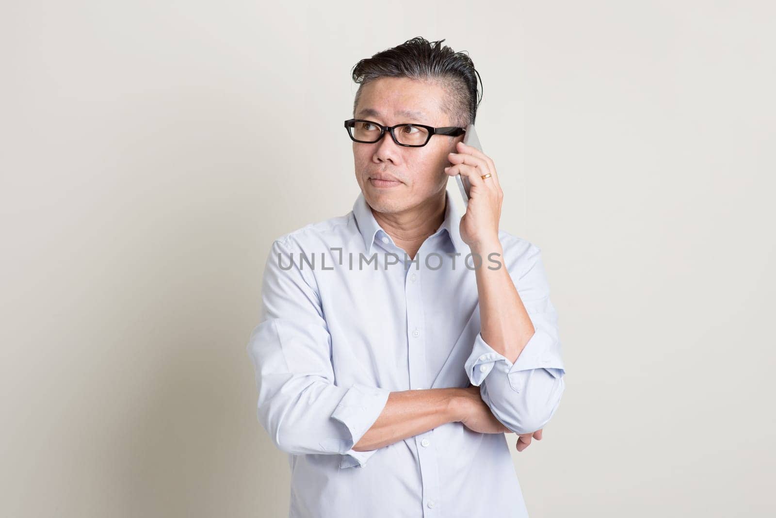Portrait of single mature 50s Asian man in casual business calling on  smartphone, standing over plain background with shadow. Chinese senior male people.