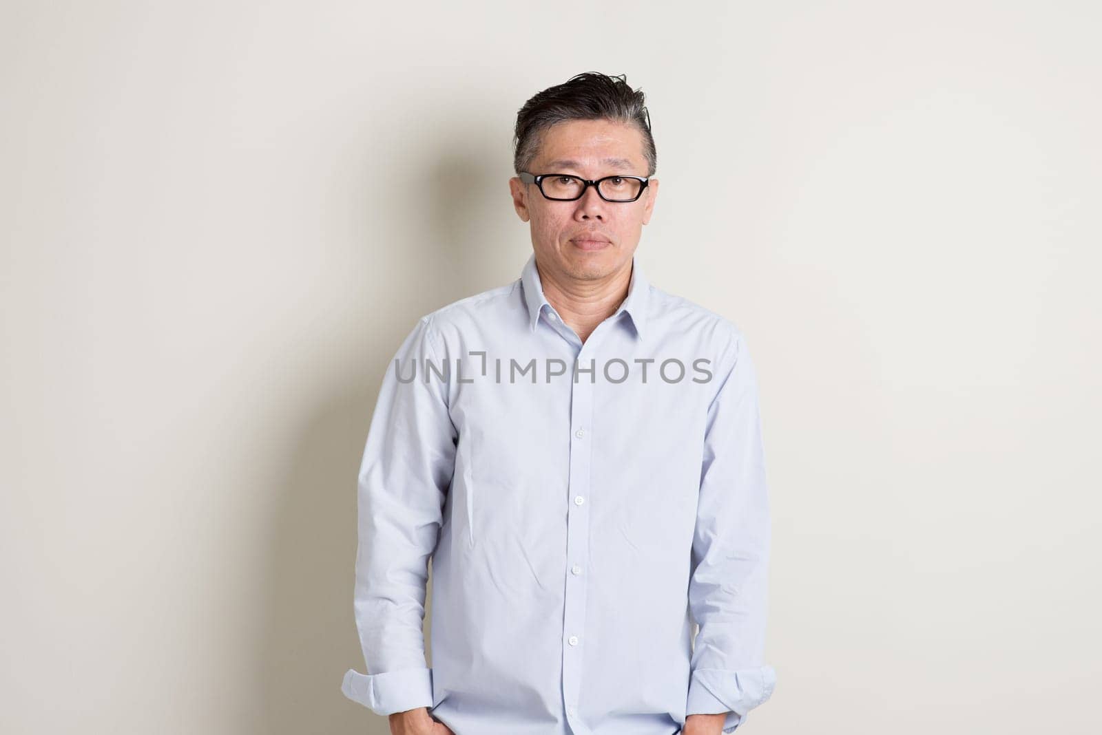 Portrait of single mature 50s Asian man in casual business standing over plain background with shadow.