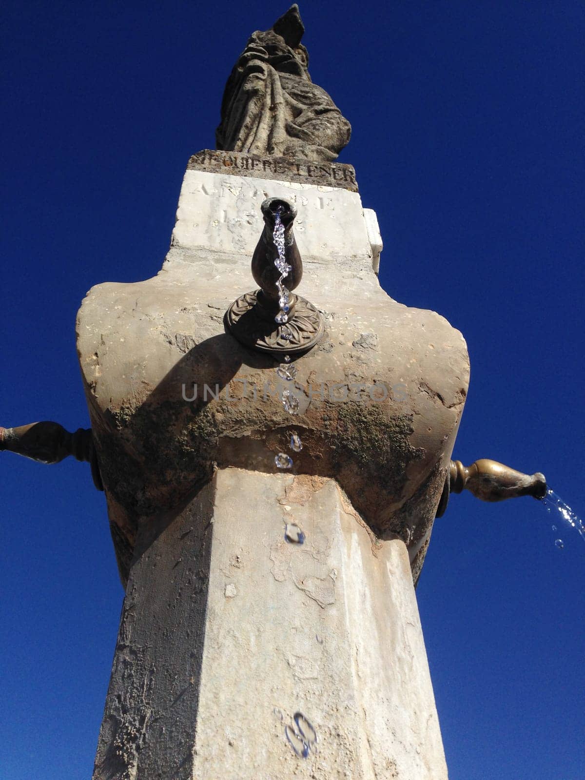 Close-up of an old stone fountain with dripping water and blue sky background. Low angle