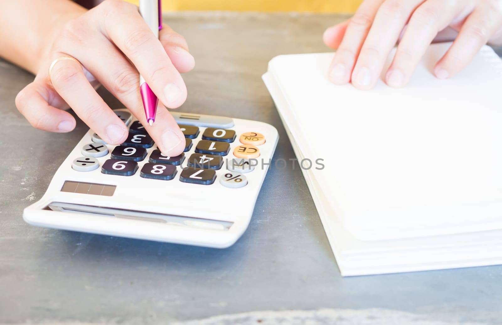 Hand holding pen and pressing calculator buttons, stock photo