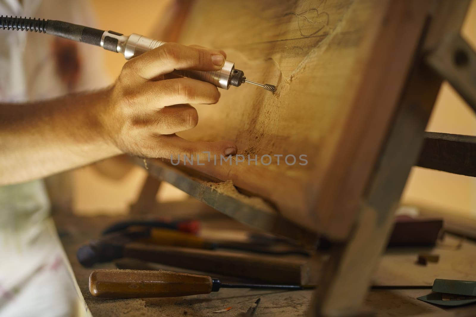 Adult man at work as artist, chiselling a bas-relief in his atelier. He works with a drill to ceasel a wood painting.