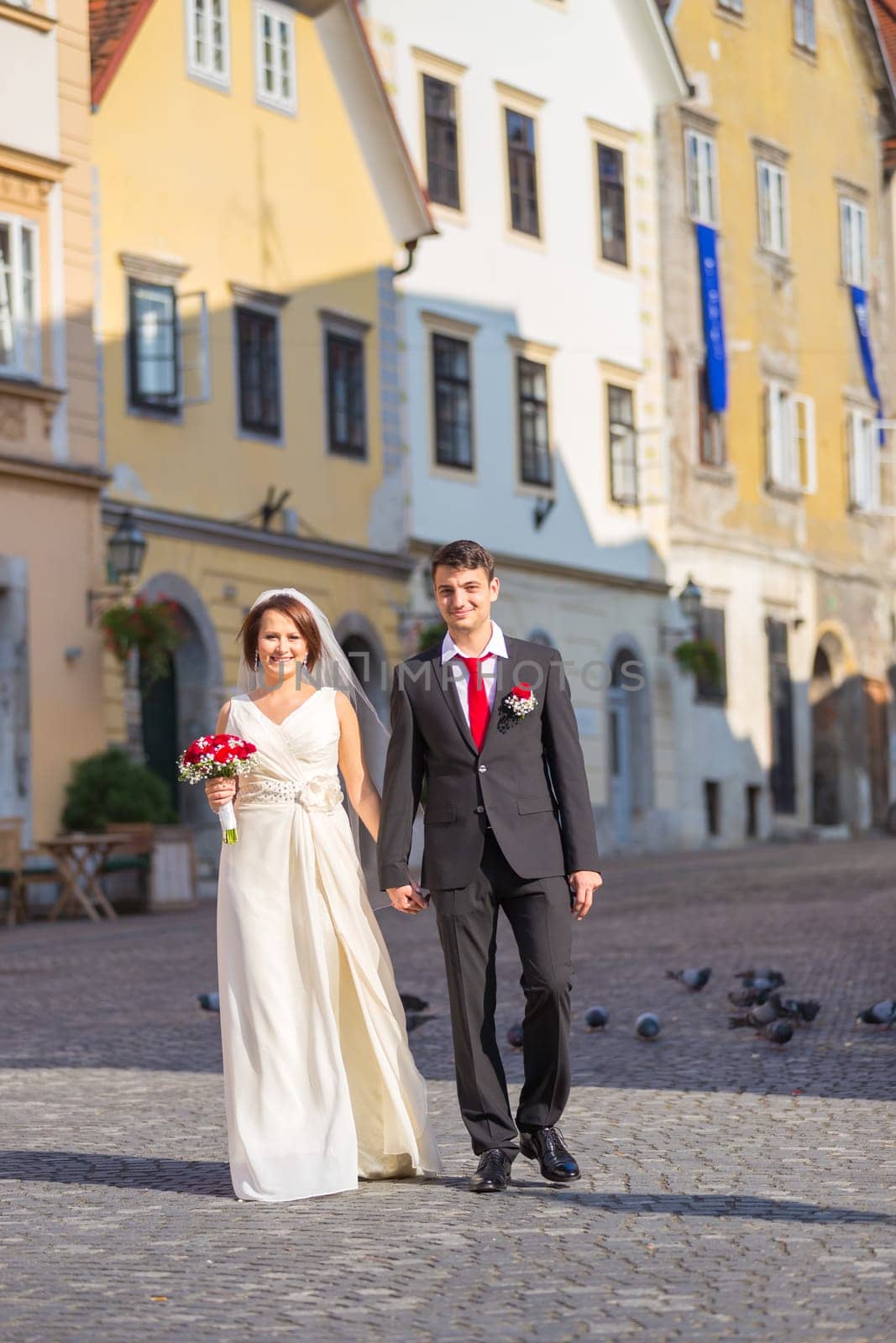 Bride and groom. Portrait of a loving wedding couple, holding hands, walking down cobbled street in medieval city center of Ljubljana, Slovenia.