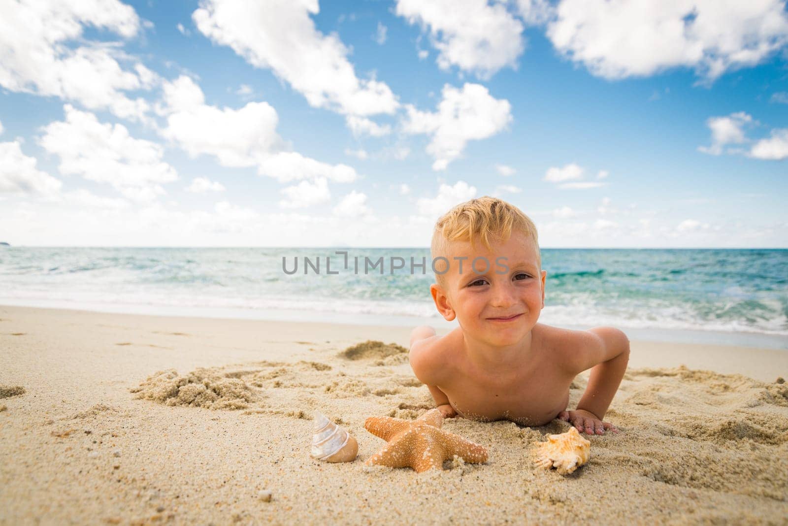 smiling little boy plays with a starfish on the beach on a summer day
