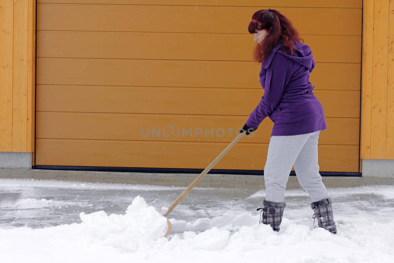 Snow clearing in winter - A woman clears snow in front of a garage