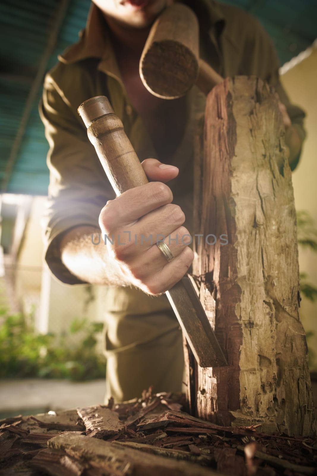 Young man at work learning craftsman profession, working with hammer and chisel. The artist carves a raw block of wood to make a wooden statue