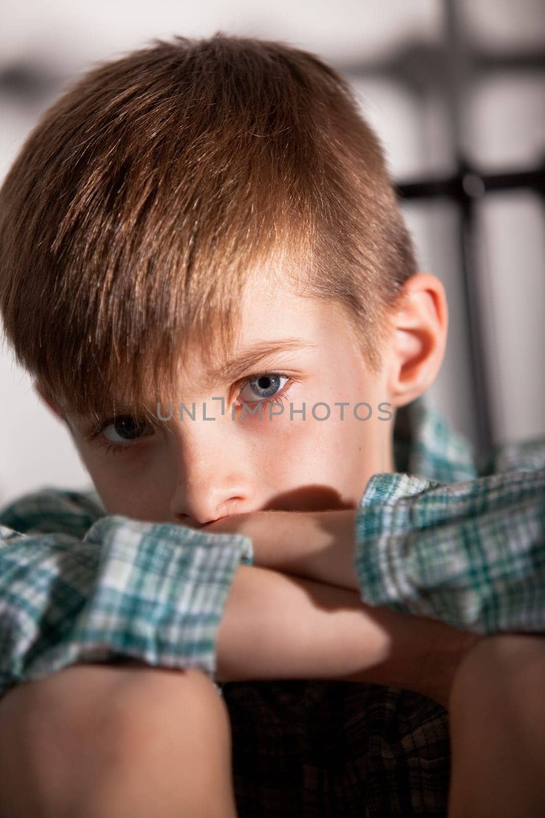 Close up Blond Young Boy with Knees Up and Folded Arms, Looking Straight at the Camera with Sad Facial Expression.