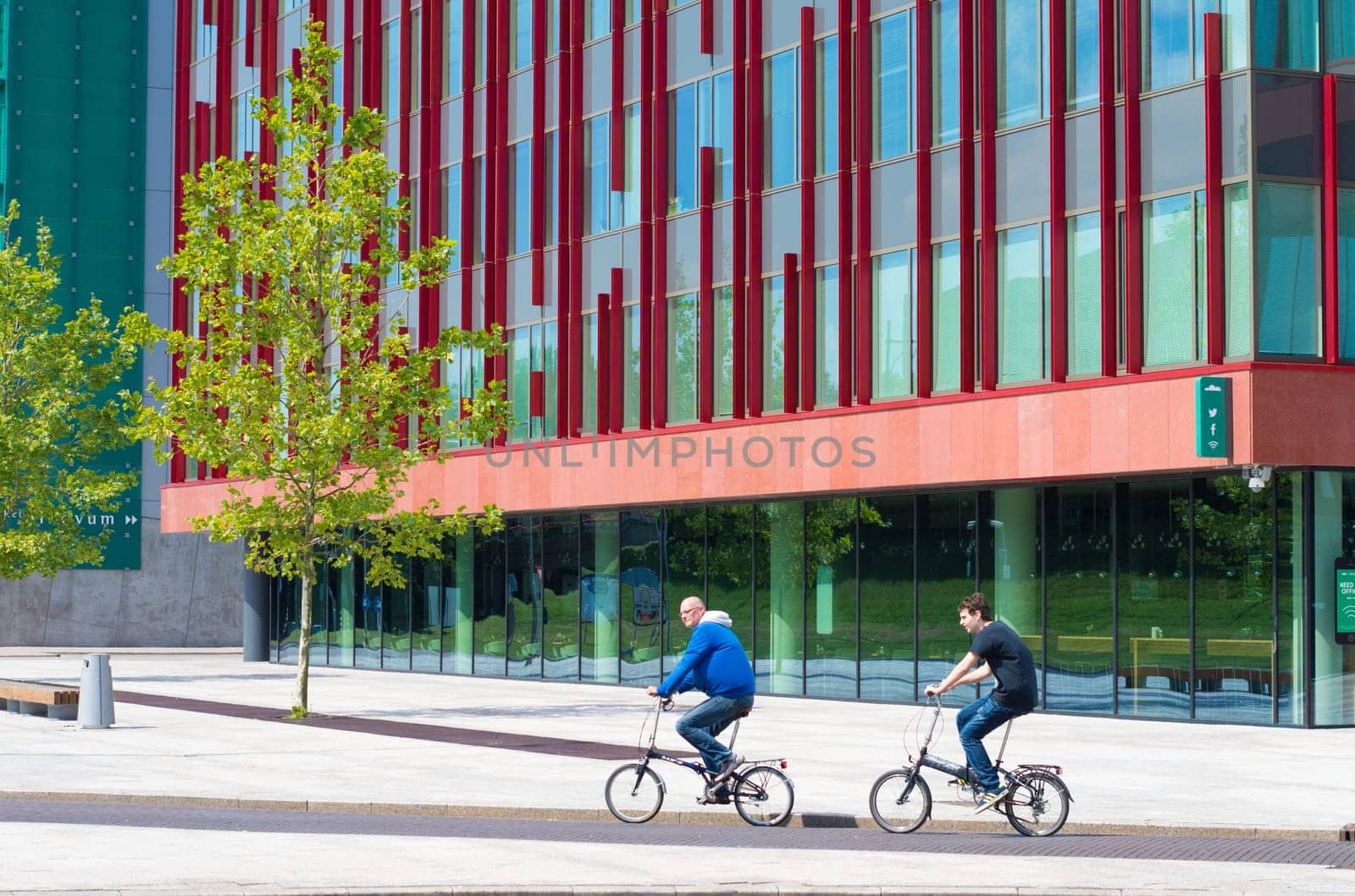 bikers passing a modern office building in Almere, netherlands. It is the youngest and fastest growing city in the country, founded around 1975.