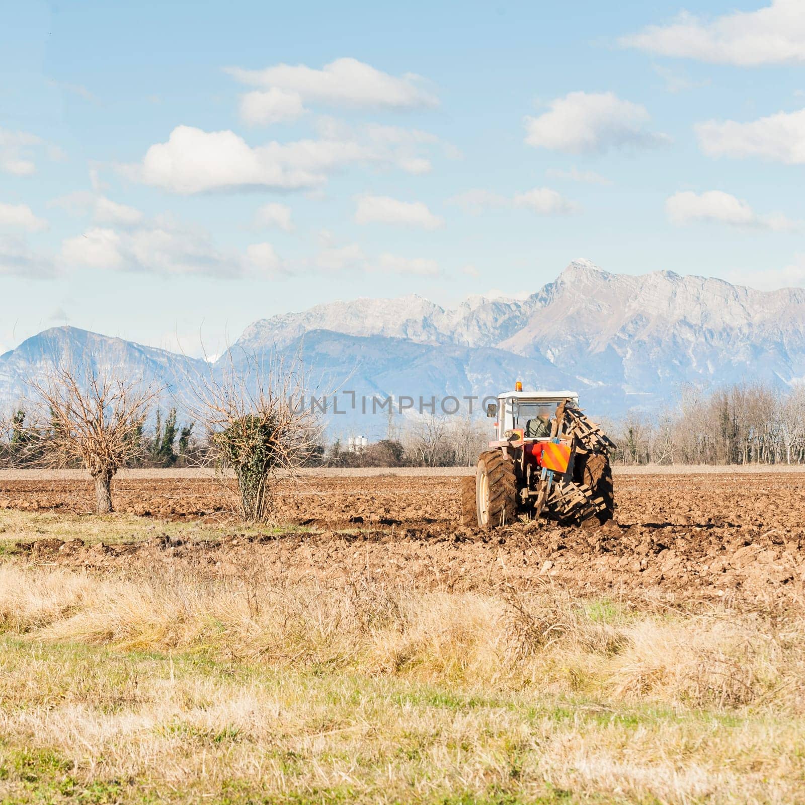 Agricultural landscape. With tractor plowing a field. The mountains in the background.