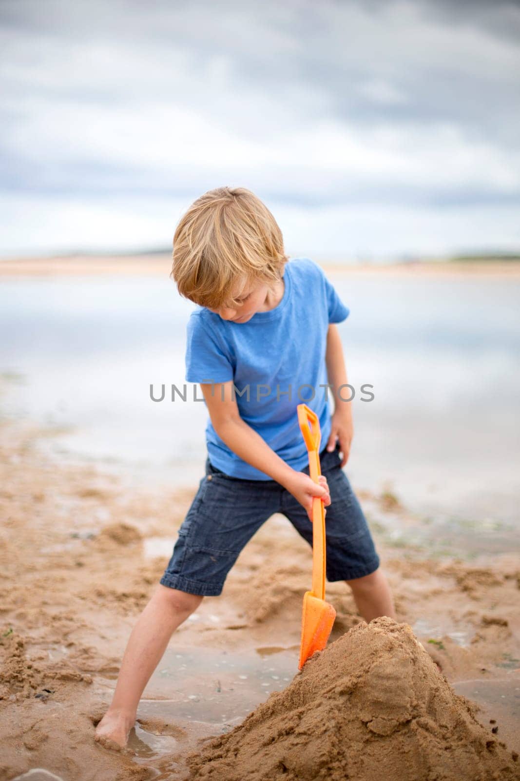 A little boy is on the beach. He is playing by himself, building sand castles.