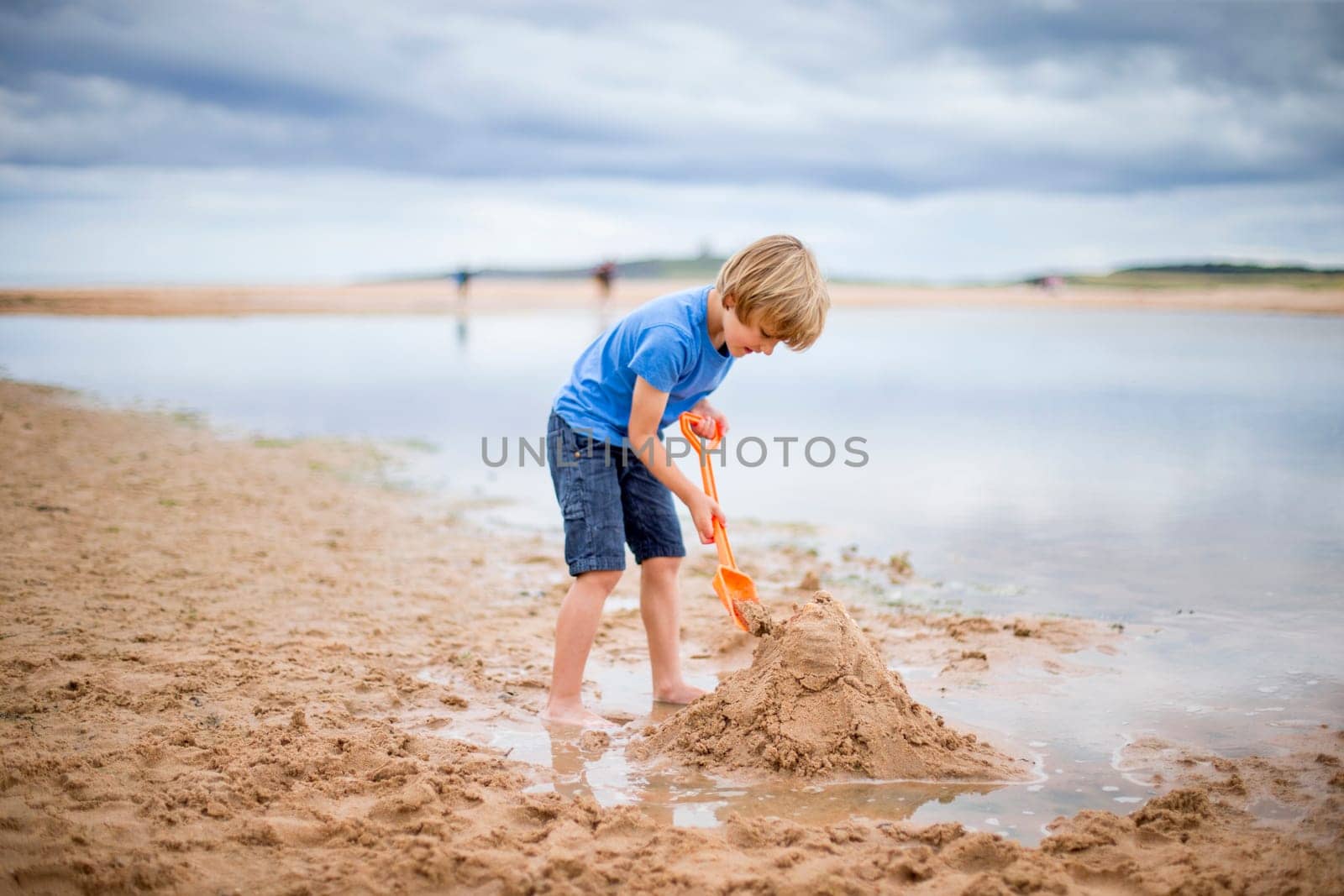A little boy is at the beach building a sand castle.