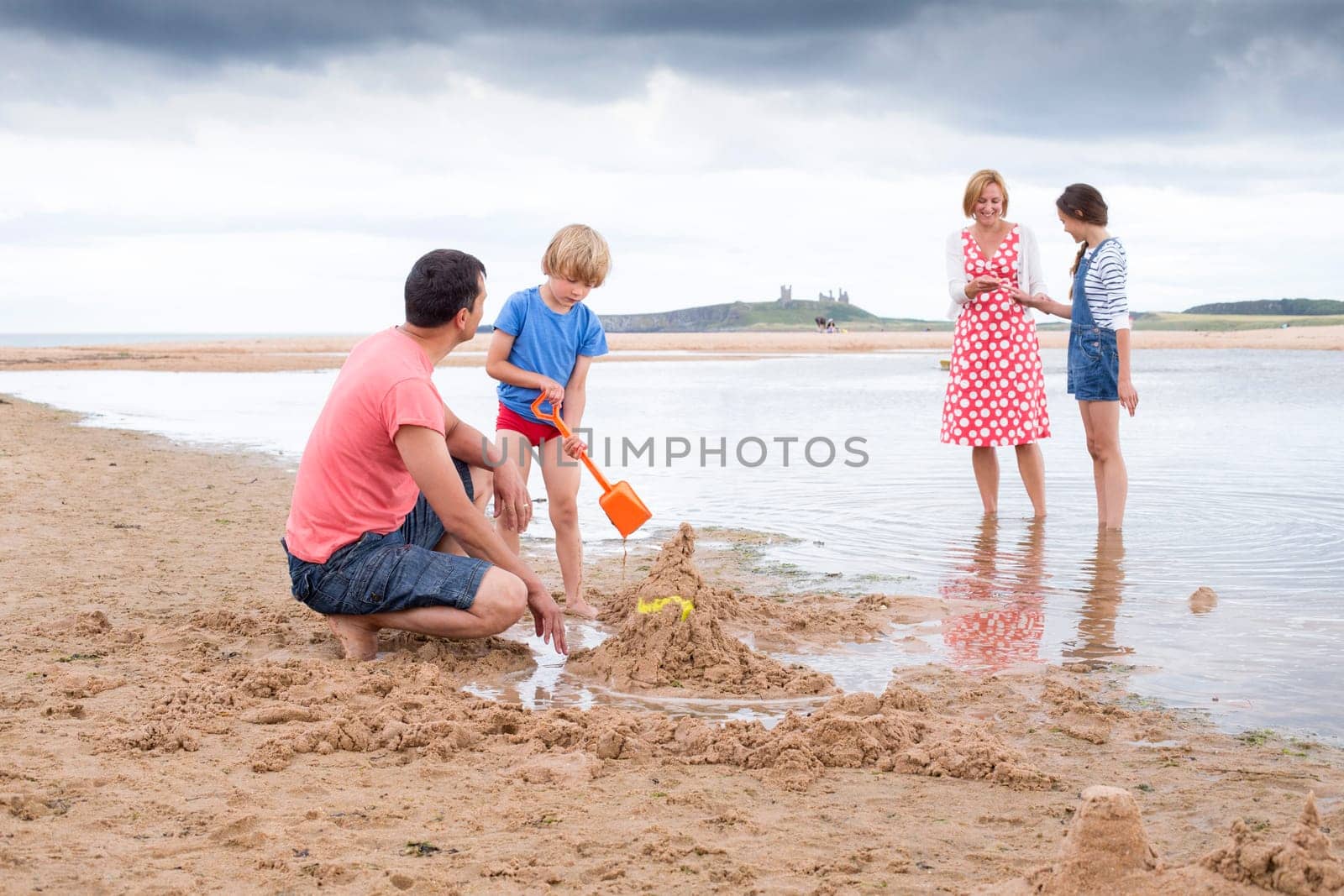 A family of four are playing on the beach together. They all look happy and are smiling.