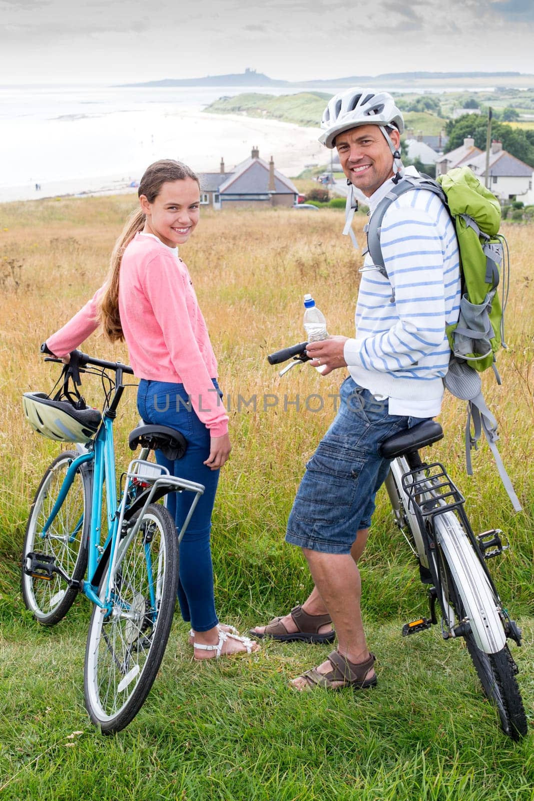 A father and daughter are sat on their bikes on the sand dunes, they are smiling and looking at the camera.