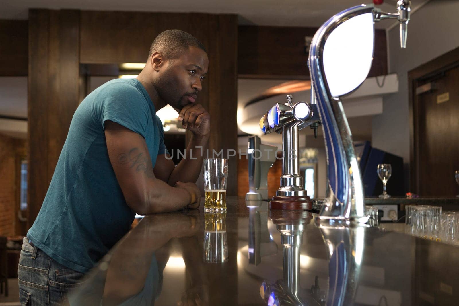 Young man standing at the bar looking deep in thought, with a pint in his hand.