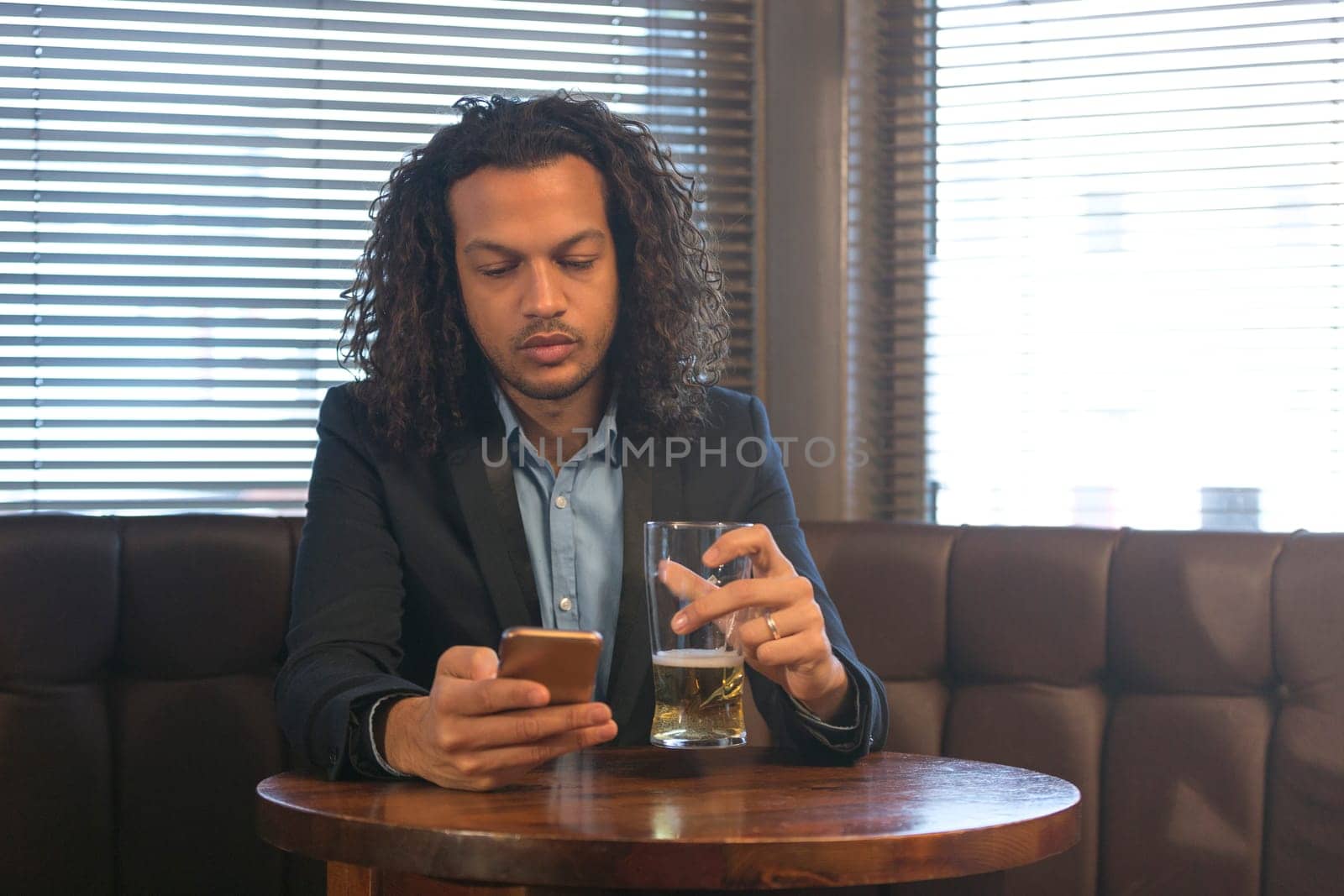 Young man using his smartphone whilst enjoying a beer in a bar.